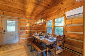 A wooden cabin interior with a dining table set for four, benches, and a hanging light fixture. - Horse Valley Lodge (Boone)