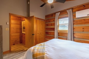 A bedroom with a wooden slat wall, a bed with a checkered blanket, a ceiling fan, and an air conditioning unit. - Horse Valley Lodge (Boone)