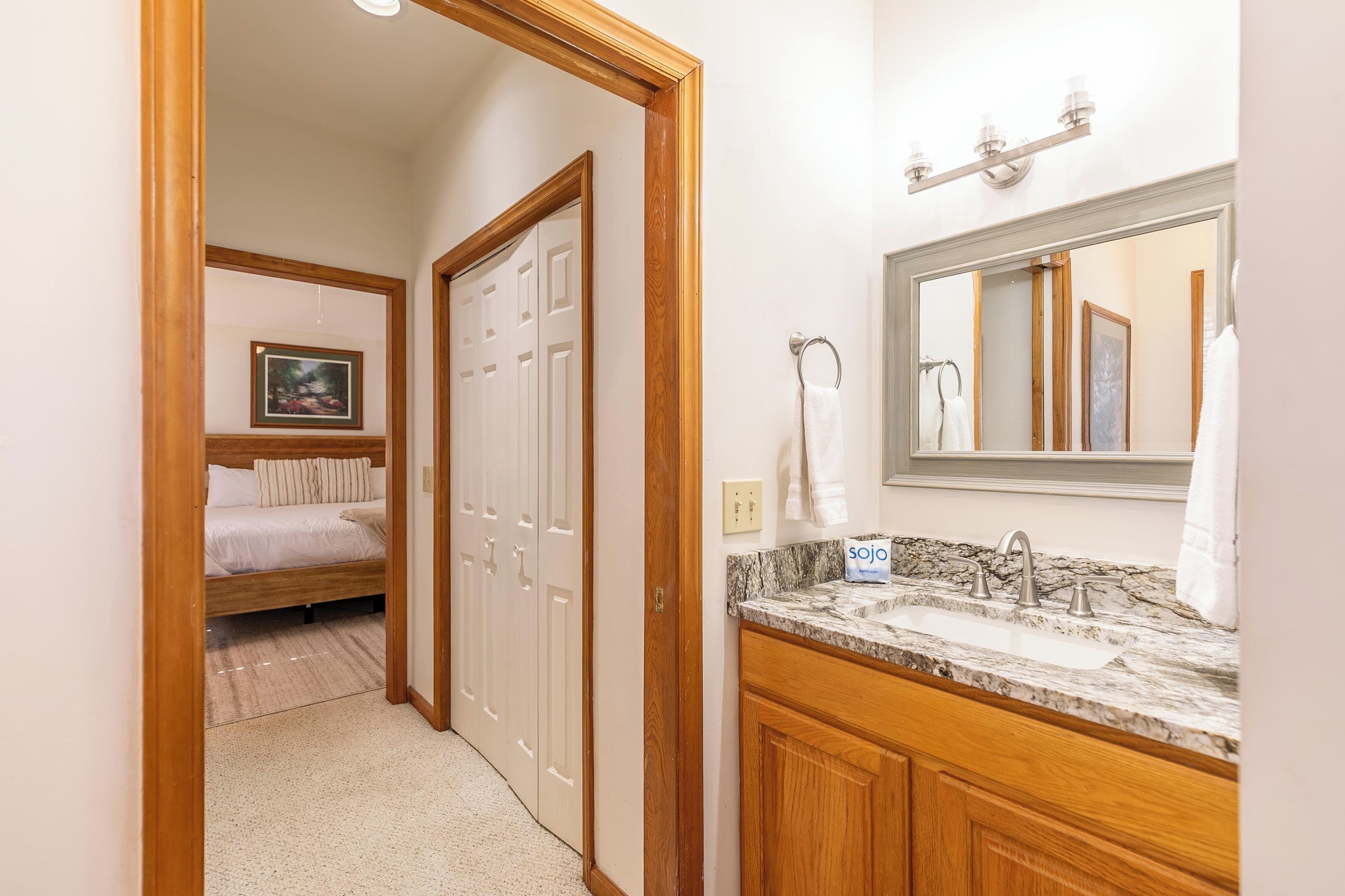 A bedroom with a bed, a wooden door, a bathroom with a sink and mirror.