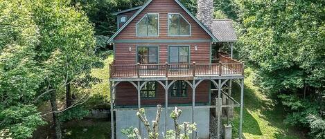 A two-story wooden cabin with a balcony, surrounded by dense forest.