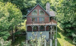 A two-story wooden cabin with a balcony, surrounded by dense forest. - A Change of Scenery at Yonahlossee 5 BR (Boone)