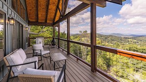 Eine Holzterrasse mit Gartenmöbeln, einem Grill und einem herrlichen Blick auf Berge und Bäume.