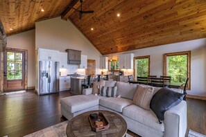 A spacious living area with a large L-shaped sectional sofa, a wooden coffee table, and a kitchen with white cabinets and stainless steel appliances. - Blue Heaven (Boone)