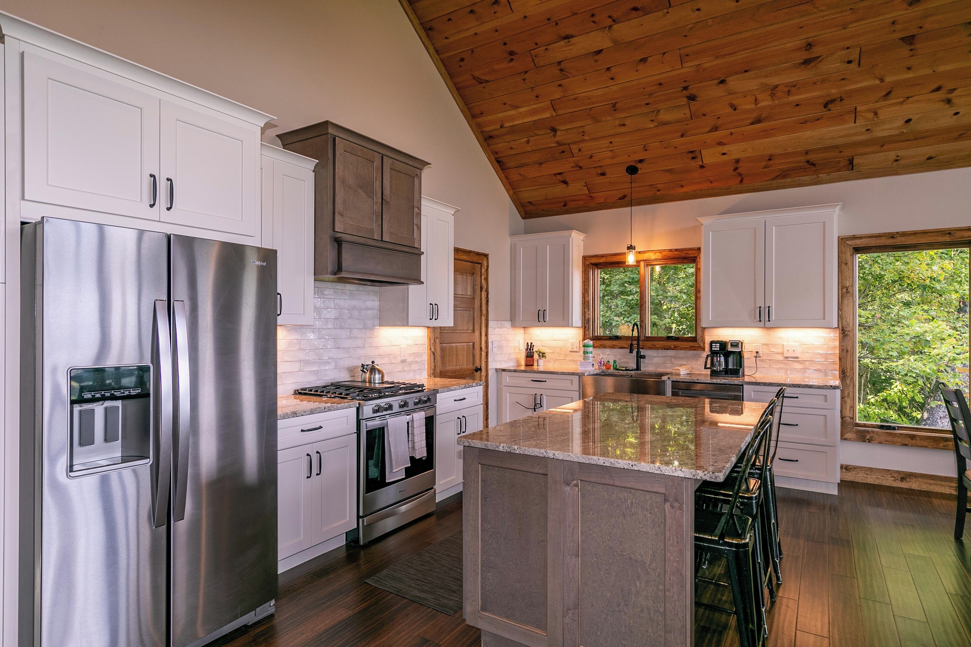 A modern kitchen with stainless steel appliances, white cabinetry, and a wooden ceiling.