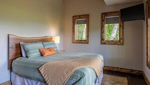 Ein Schlafzimmer mit Bett, zwei Fenstern, einem Fernseher und einem Holzkopfende.