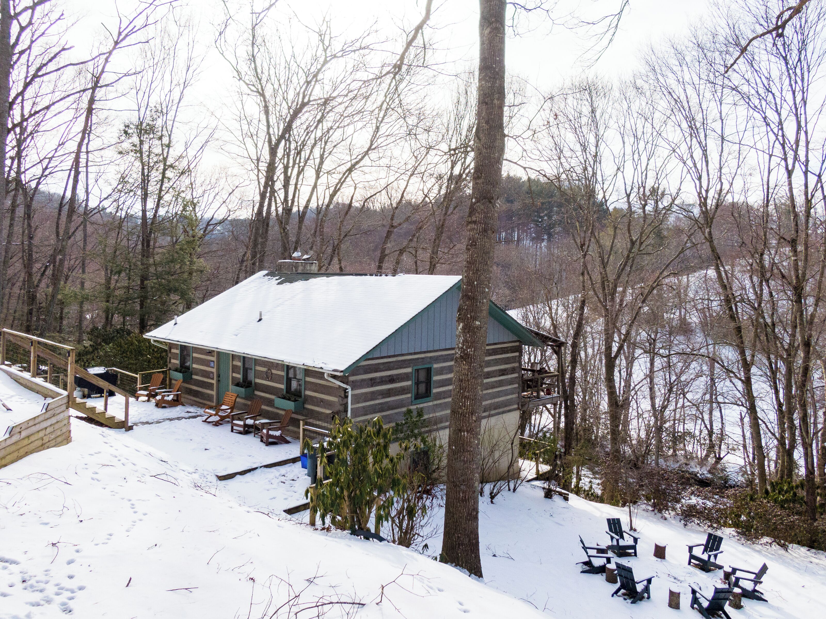 A log cabin with a snow-covered roof, outdoor seating, and a view of a forested area.