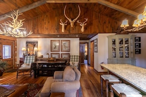 A rustic interior with wooden walls, a dining area, a sofa, and a cabinet with glass doors. - Riverdale - 4BR With a hot Tub- Near the New River (Boone)
