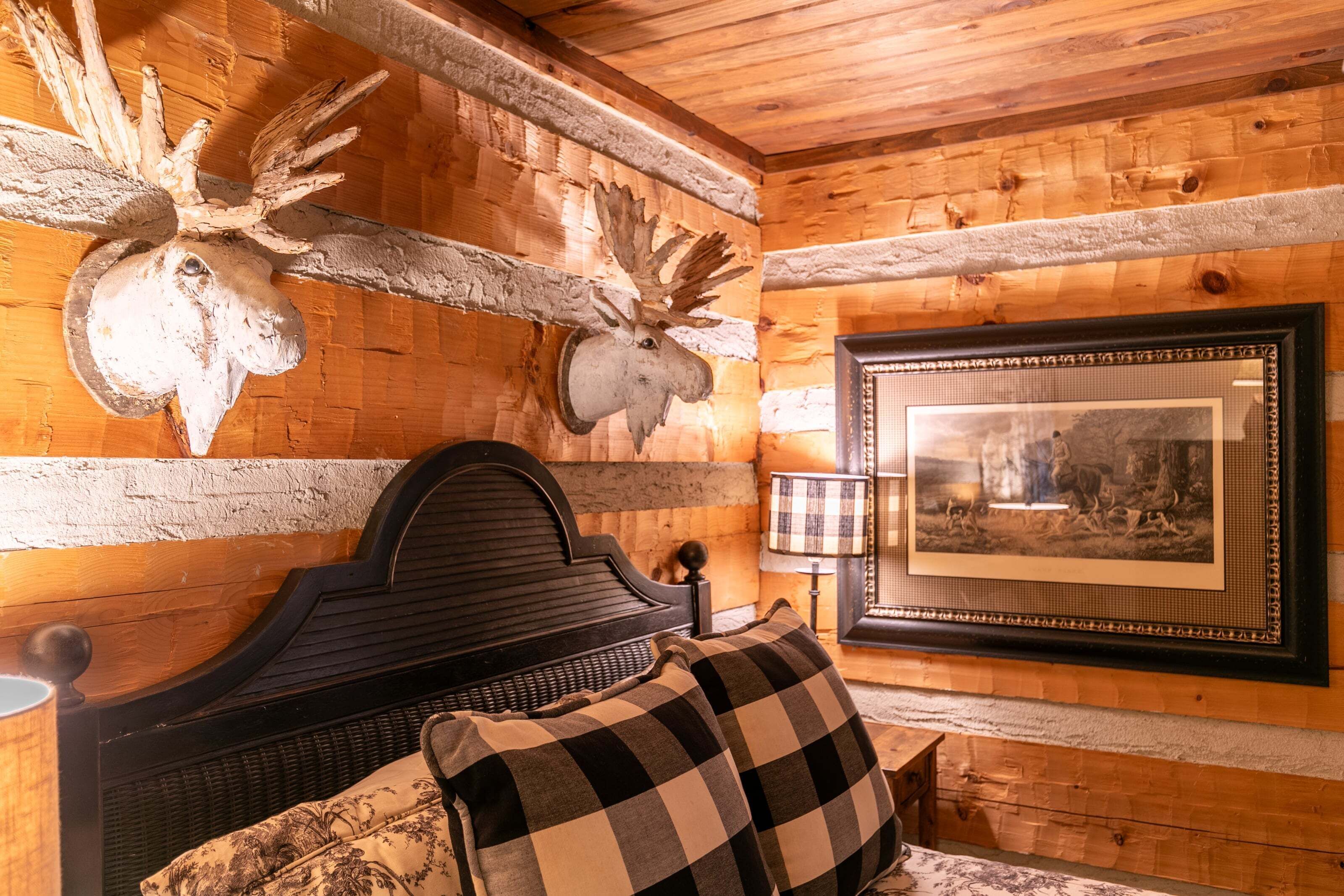 A wooden cabin interior with a bed, a mounted moose head, and a framed picture on the wall.