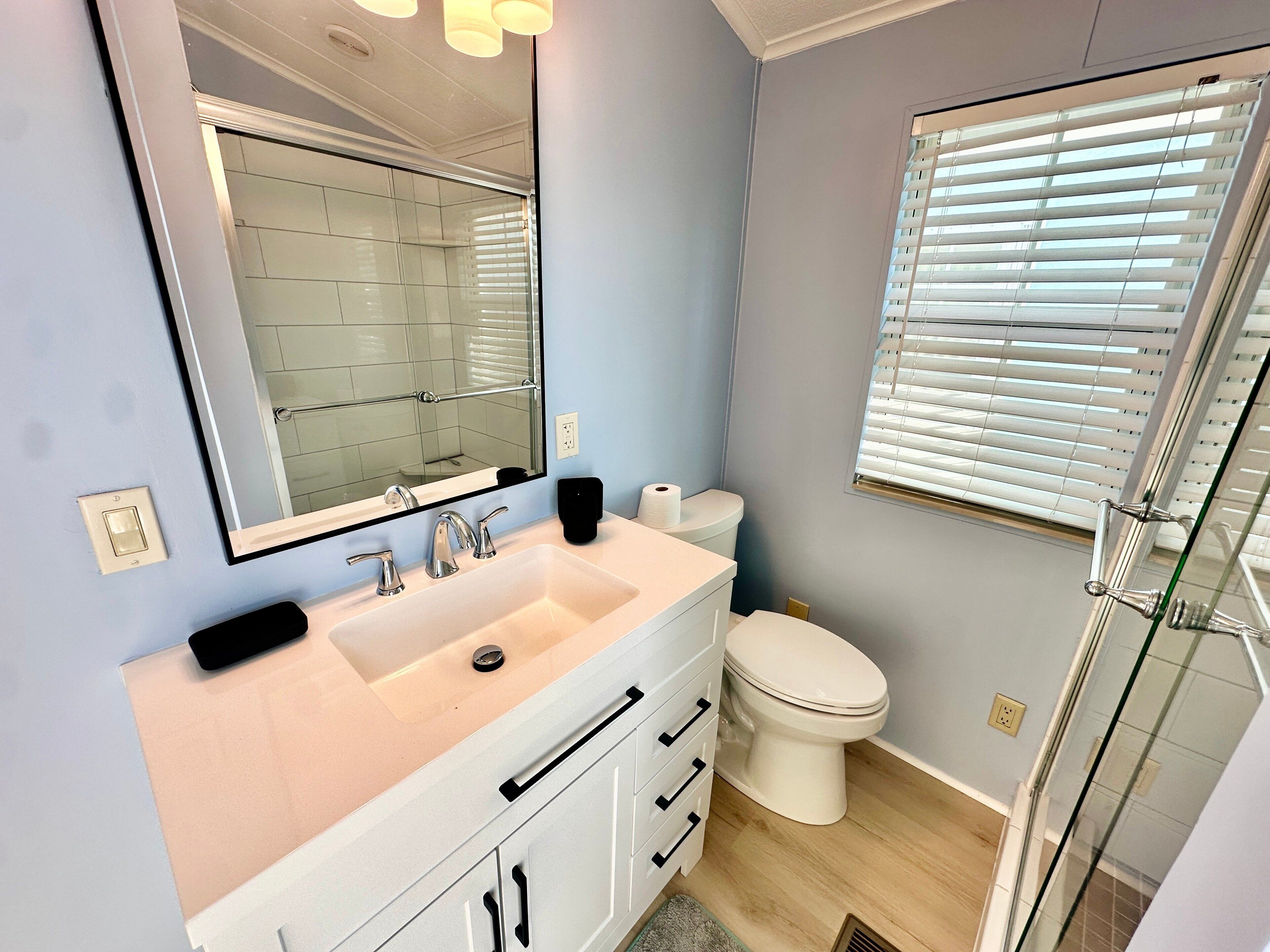 Un baño moderno con tocador blanco, un espejo grande, un inodoro y una cabina de ducha de vidrio.