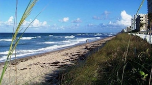 Una playa con olas, una persona caminando y edificios al fondo.
