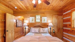 Ein Zimmer einer Holzhütte mit einem Bett, gerahmten Pflanzenbildern an der Wand und einem Deckenventilator.