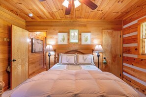 Ein Zimmer einer Holzhütte mit einem Bett, gerahmten Pflanzenbildern an der Wand und einem Deckenventilator.