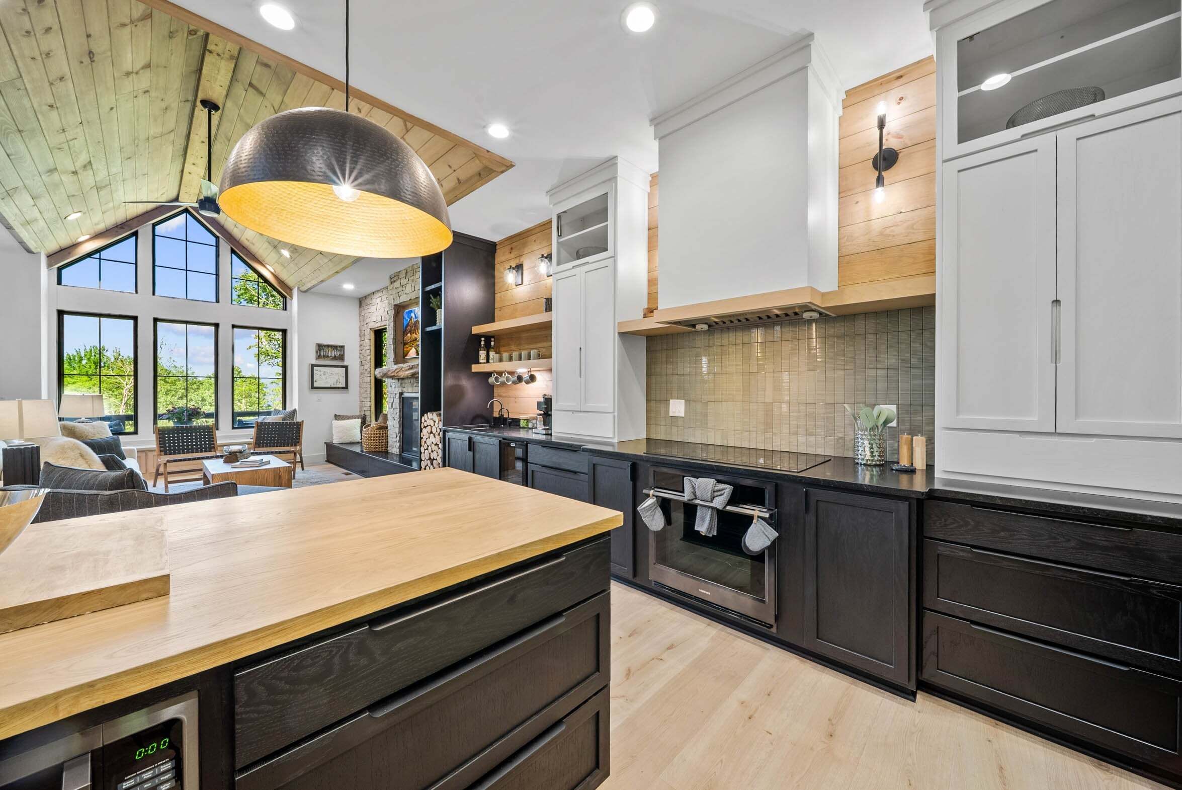 A modern kitchen with dark cabinetry, a wooden island, and a large window.