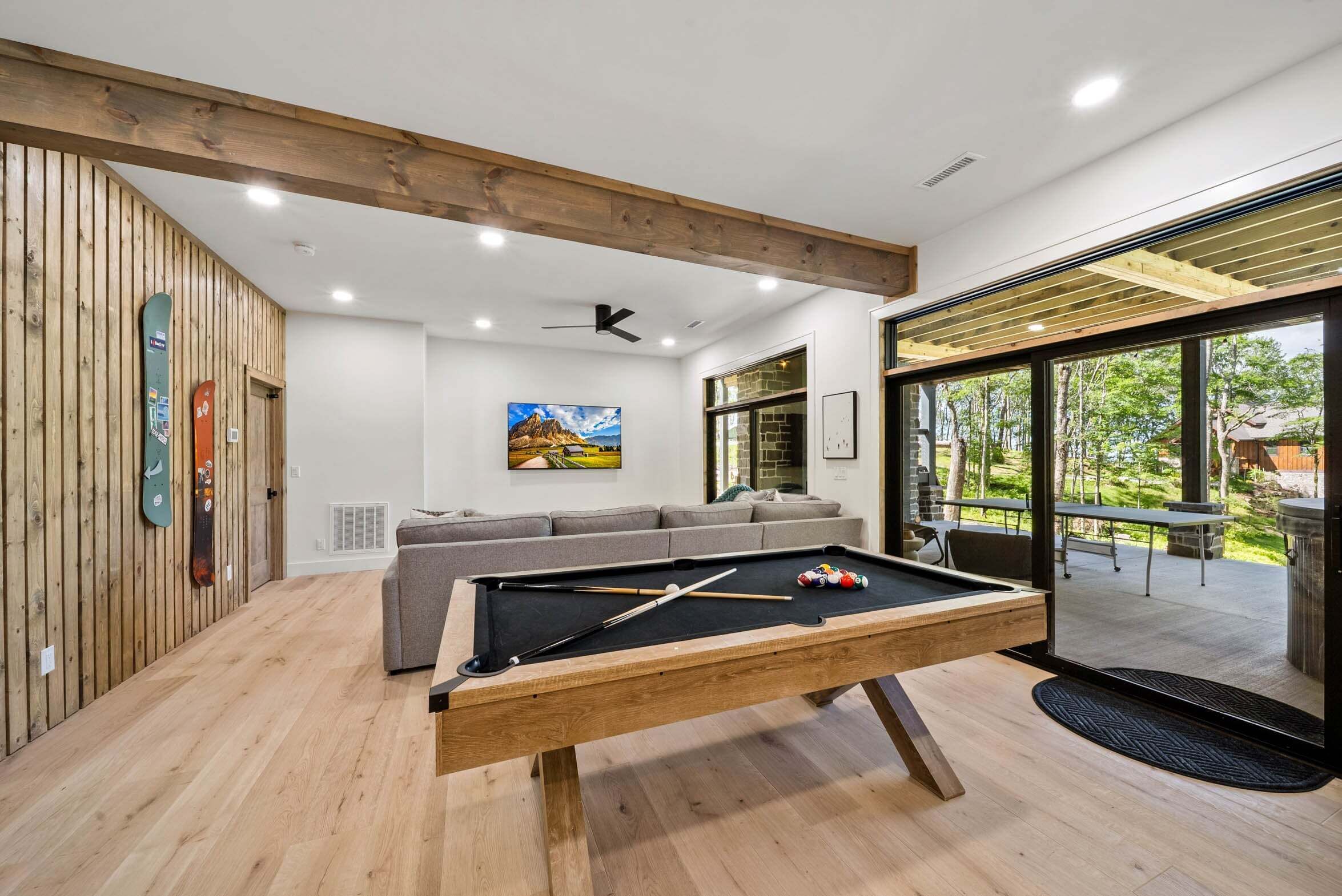 A modern indoor pool table with a wooden finish, a grey sofa, and a painting on the wall.