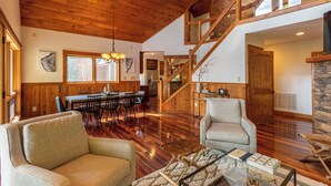 A spacious living area with wooden floors, a dining table, and a staircase leading to an upper level. - Shady Pines (Banner Elk)