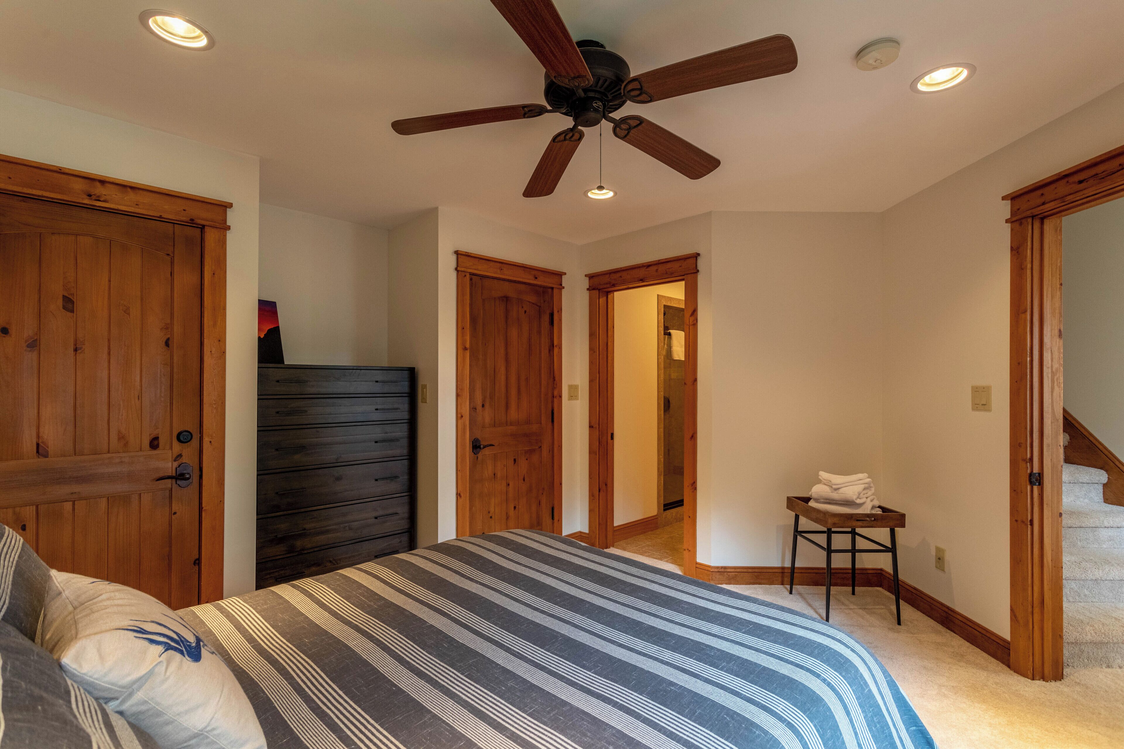 A bedroom with a bed, wooden doors, a ceiling fan, and a small table with towels.