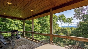 A wooden deck with a table and chairs, overlooking a forested area with mountains in the distance. - Shady Pines (Banner Elk)