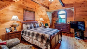 Un dormitori d'una cabana de fusta acollidora, amb un llit, dues taules de nit, un tocador, una televisió i una finestra amb vistes.