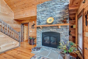 A log cabin interior with a stone fireplace, wooden staircase, and rustic decor.