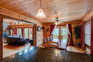 Interior de una cabaña de madera con comedor, chimenea y vistas al exterior.