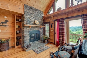 Interior acogedor de una cabaña con chimenea de piedra, estantes de madera y un balcón con vistas panorámicas.