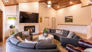 A modern living room with a curved gray sectional sofa, a fireplace, and a large flat-screen TV. - Sweet Water Estate (Butler)