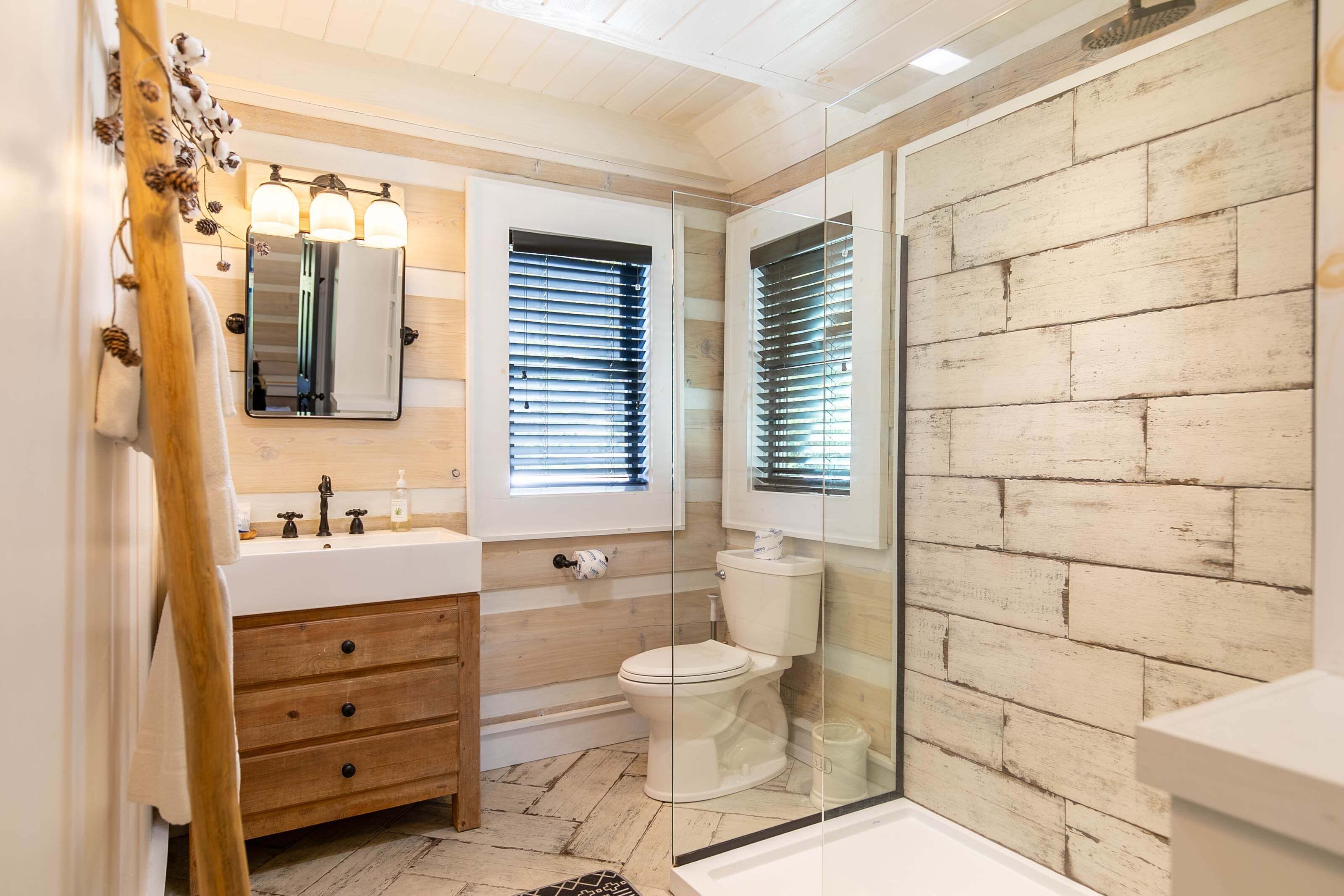 A bathroom with a wooden vanity, a toilet, and a glass shower enclosure.