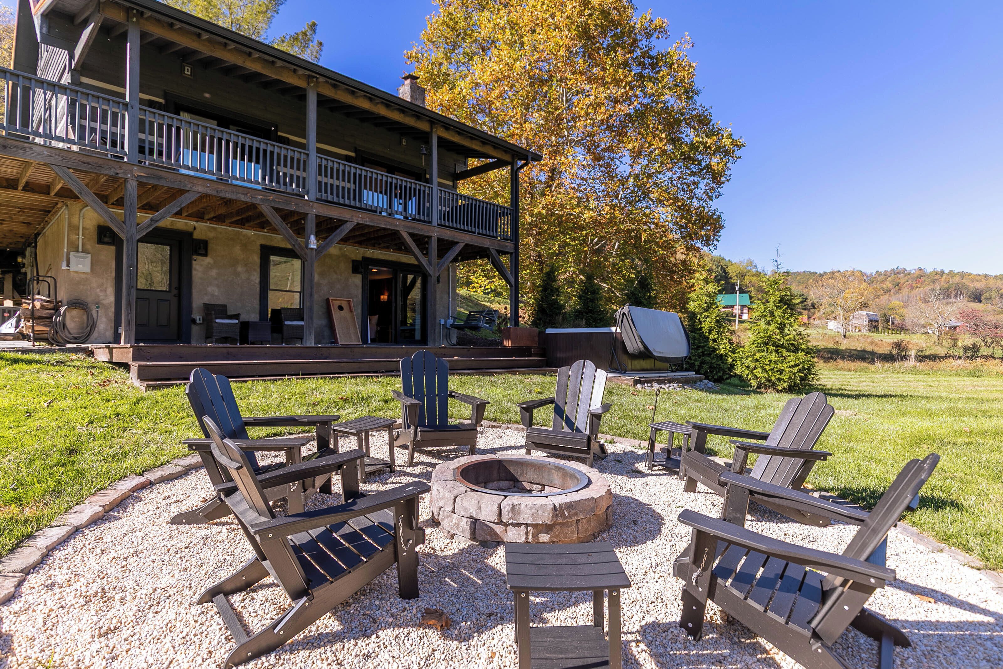 Eine Holzterrasse mit Adirondack-Stühlen und einer Feuerstelle, eine überdachte Veranda und Blick auf einen bewaldeten Hügel.