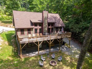 Ein zweistöckiges Haus mit einer Terrasse, Sitzgelegenheiten im Freien und einer Feuerstelle.