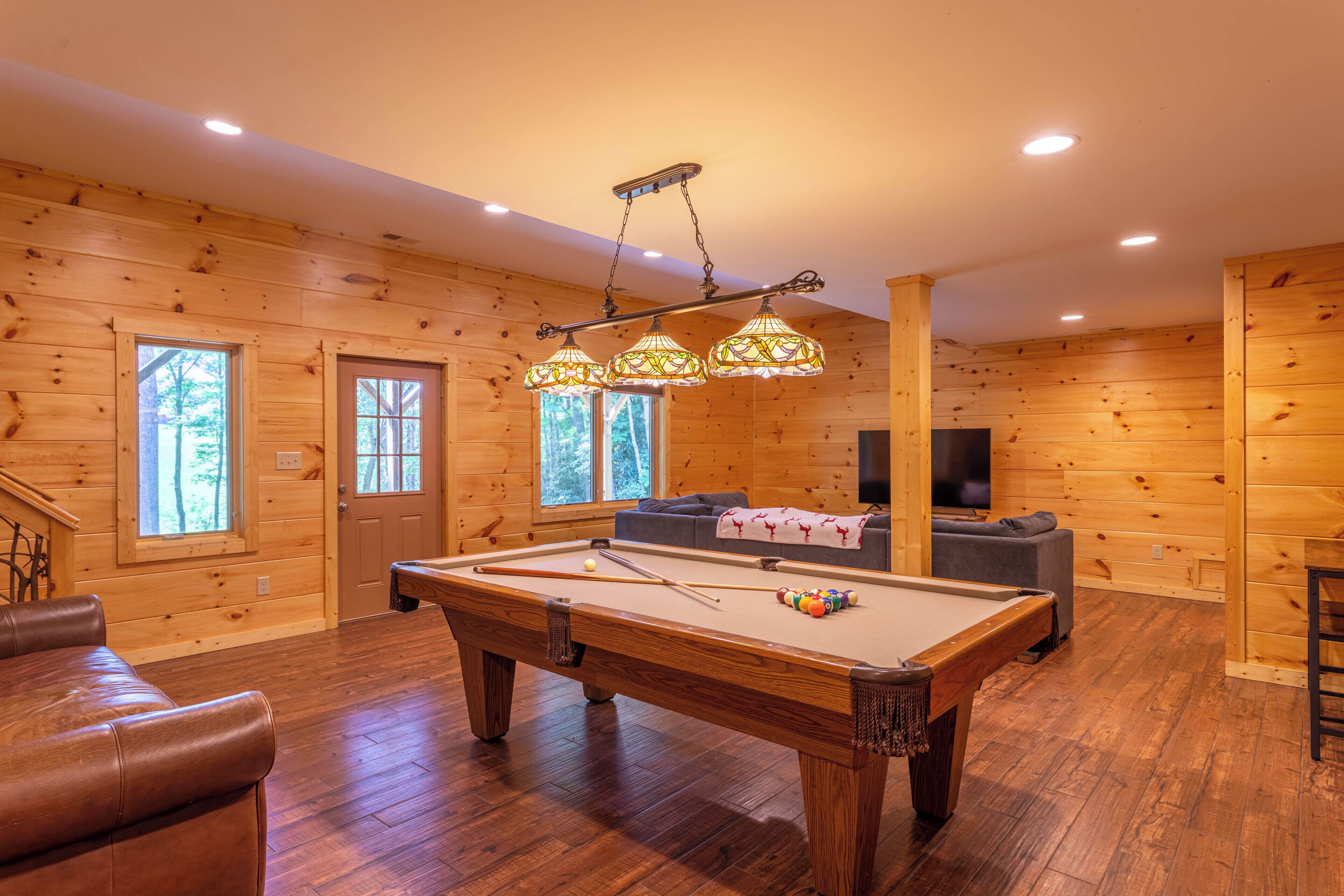 A wooden-paneled room with a pool table, a sofa, and a television.