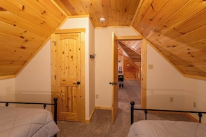Ein Schlafzimmer mit schrägem Dach, Holztür und einem sichtbaren Flur, der in ein weiteres Zimmer führt.