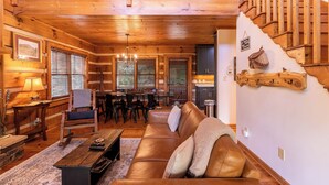 A wooden cabin interior with a dining area, a sofa, and a staircase. - Appalachian Seasons Hot tub Fire Place Seasonal Views (Banner Elk)