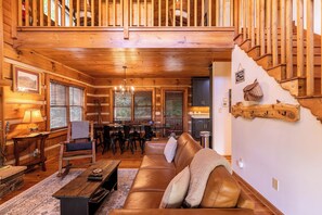 A wooden cabin interior with a dining area, a sofa, and a staircase. - Appalachian Seasons Hot tub Fire Place Seasonal Views (Banner Elk)
