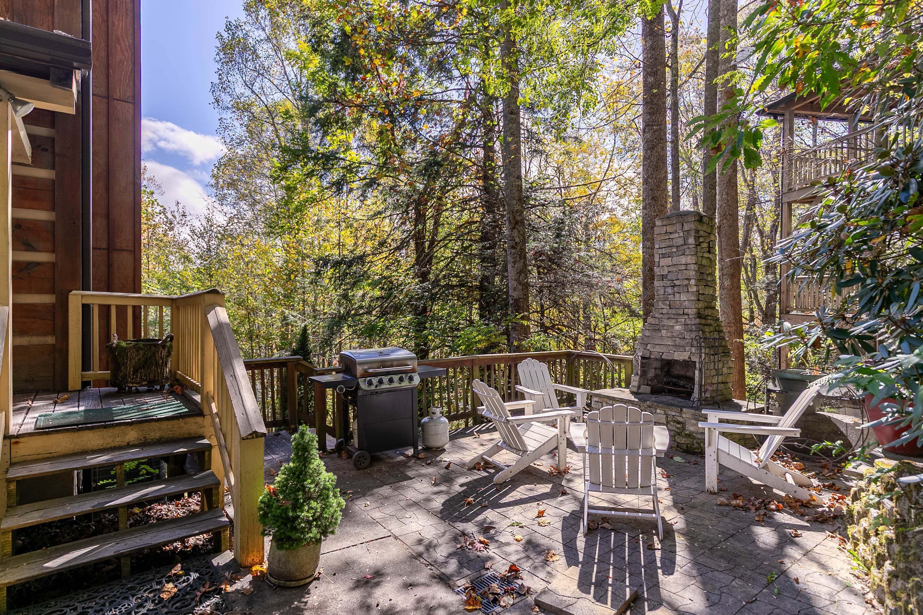 A patio with Adirondack chairs, a grill, and a stone fireplace.