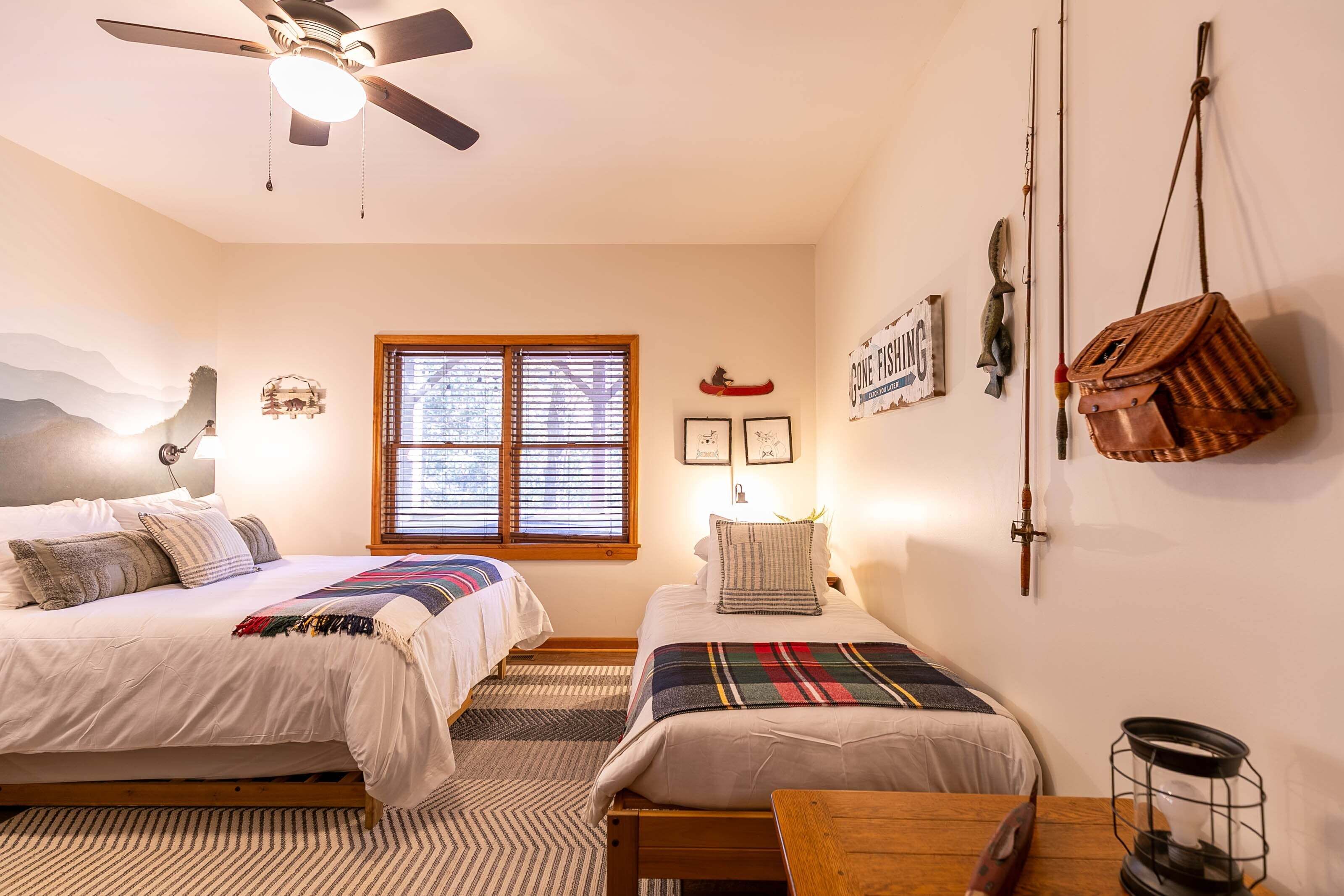 A bedroom with two beds, a ceiling fan, a window, and a wall-mounted fishing rod.