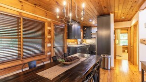 A wooden interior with a dining table, chairs, a chandelier, and a kitchen area. - Appalachian Seasons Hot tub Fire Place Seasonal Views (Banner Elk)