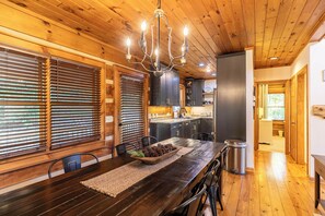 A wooden interior with a dining table, chairs, a chandelier, and a kitchen area. - Appalachian Seasons Hot tub Fire Place Seasonal Views (Banner Elk)
