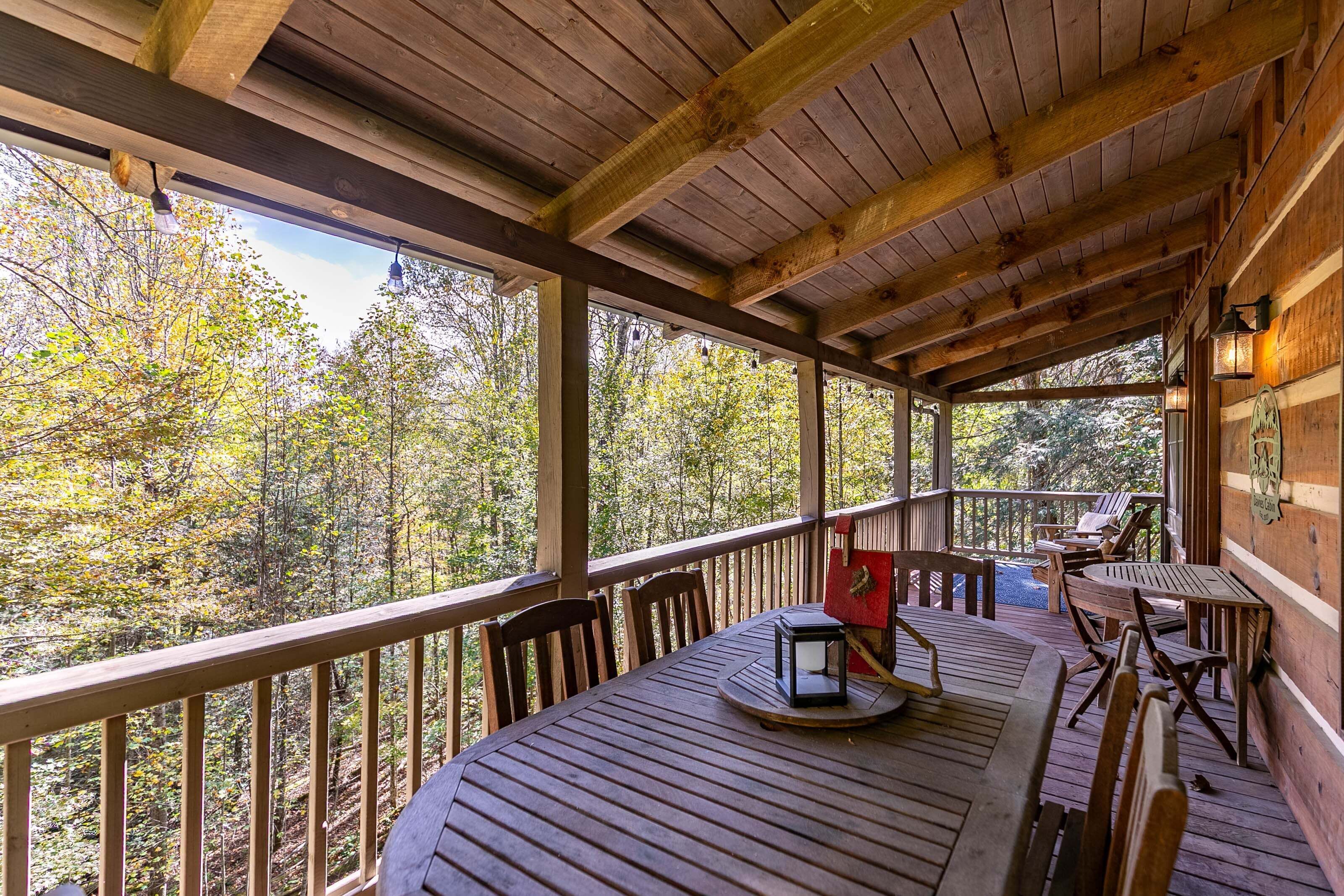 A wooden deck with tables and chairs, overlooking a forested area.