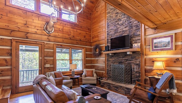 A log cabin interior with a fireplace, wooden walls, a sofa, a rocking chair, and a television. - Appalachian Seasons Hot tub Fire Place Seasonal Views (Banner Elk)