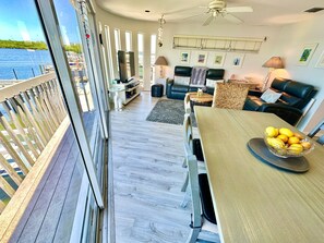 Ein Balkon mit Blick auf das Wasser, ein Essbereich mit Tisch und Stühlen sowie ein Wohnzimmer mit Sofa und Fernseher.
