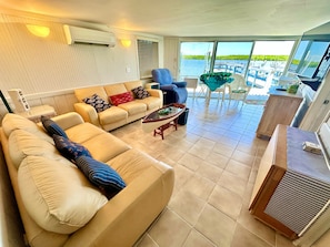 Ein geräumiges Wohnzimmer mit einer großen Couch, einem Couchtisch und Blick auf das Wasser durch bodentiefe Fenster.