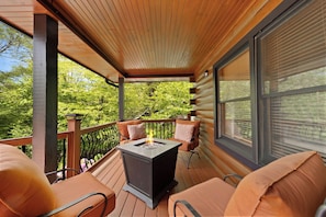 Eine überdachte Terrasse mit Kamin, Sitzgelegenheiten und großen Fenstern.