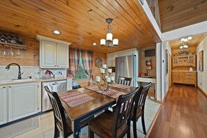 Techo de madera, una mesa de comedor con sillas, una cocina con armarios, un refrigerador y un televisor.