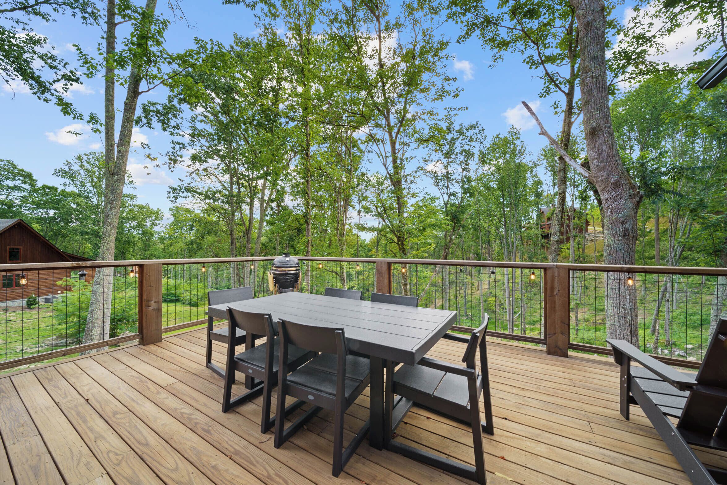 A wooden deck with a table and chairs, surrounded by trees and a clear sky.