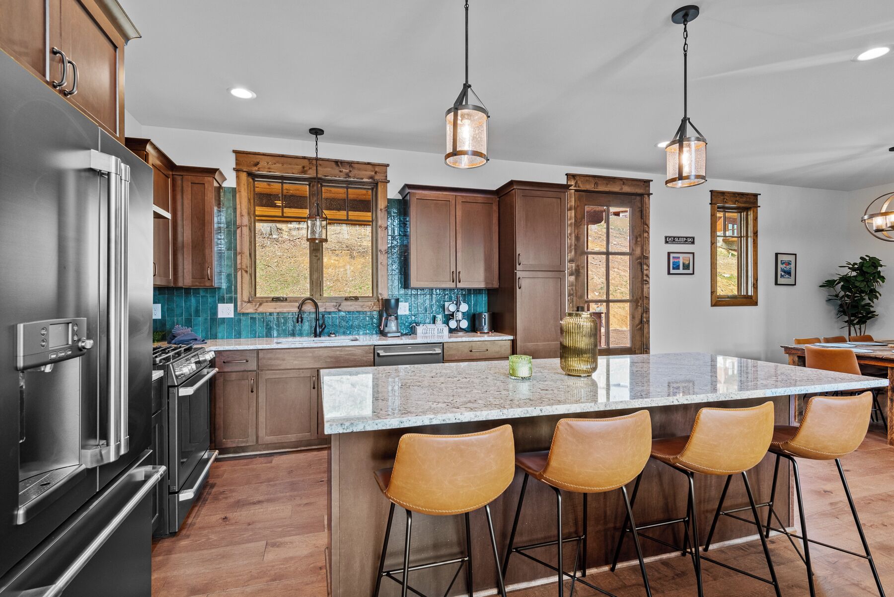 A modern kitchen with stainless steel appliances, wooden cabinets, a large island with bar stools, and pendant lighting.
