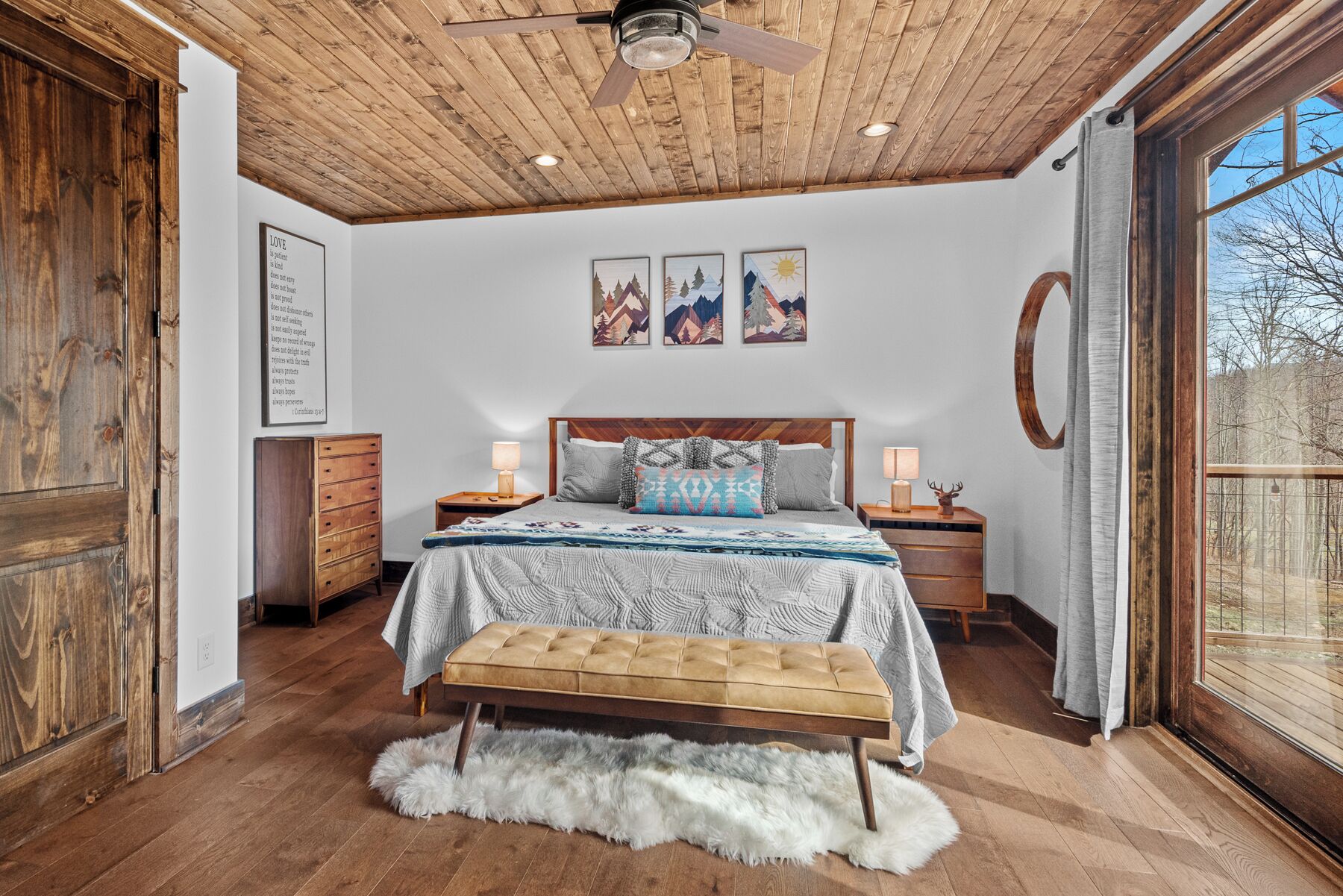 A bedroom with a wooden ceiling, a bed with a patterned bedspread, a bench, and a fur rug.