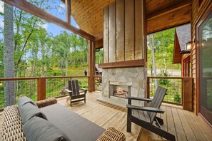 Une terrasse en bois avec une cheminée en pierre, un coin salon extérieur et une vue sur la forêt.