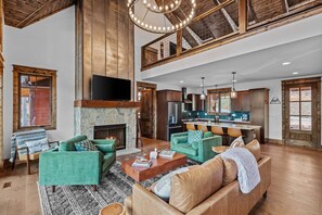 A spacious living area with a fireplace, a kitchen with a bar, and a high ceiling with exposed beams. - Llama Creek Cabin at Eagles Nest (Banner Elk)