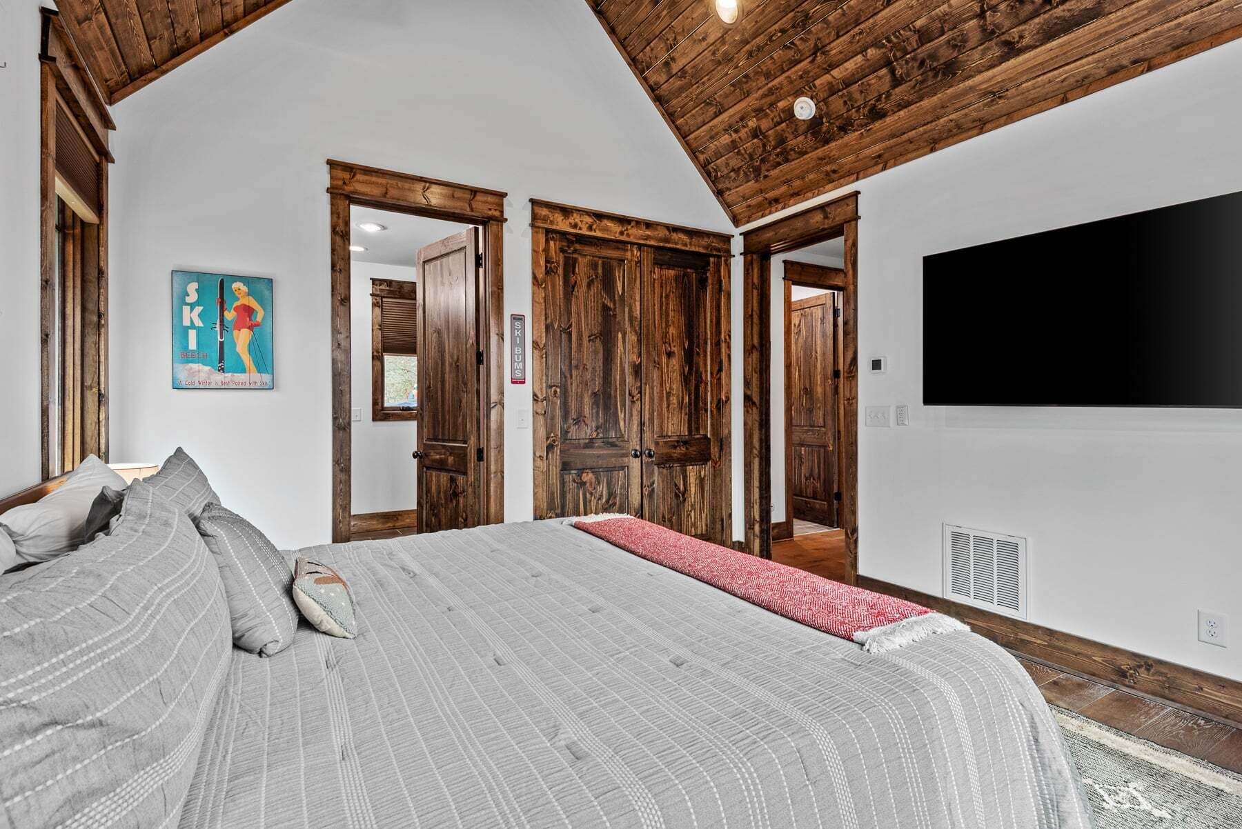 Ein Schlafzimmer mit einem großen Bett, Holztüren, einem Fernseher und einem Wandbild zum Thema Skifahren.