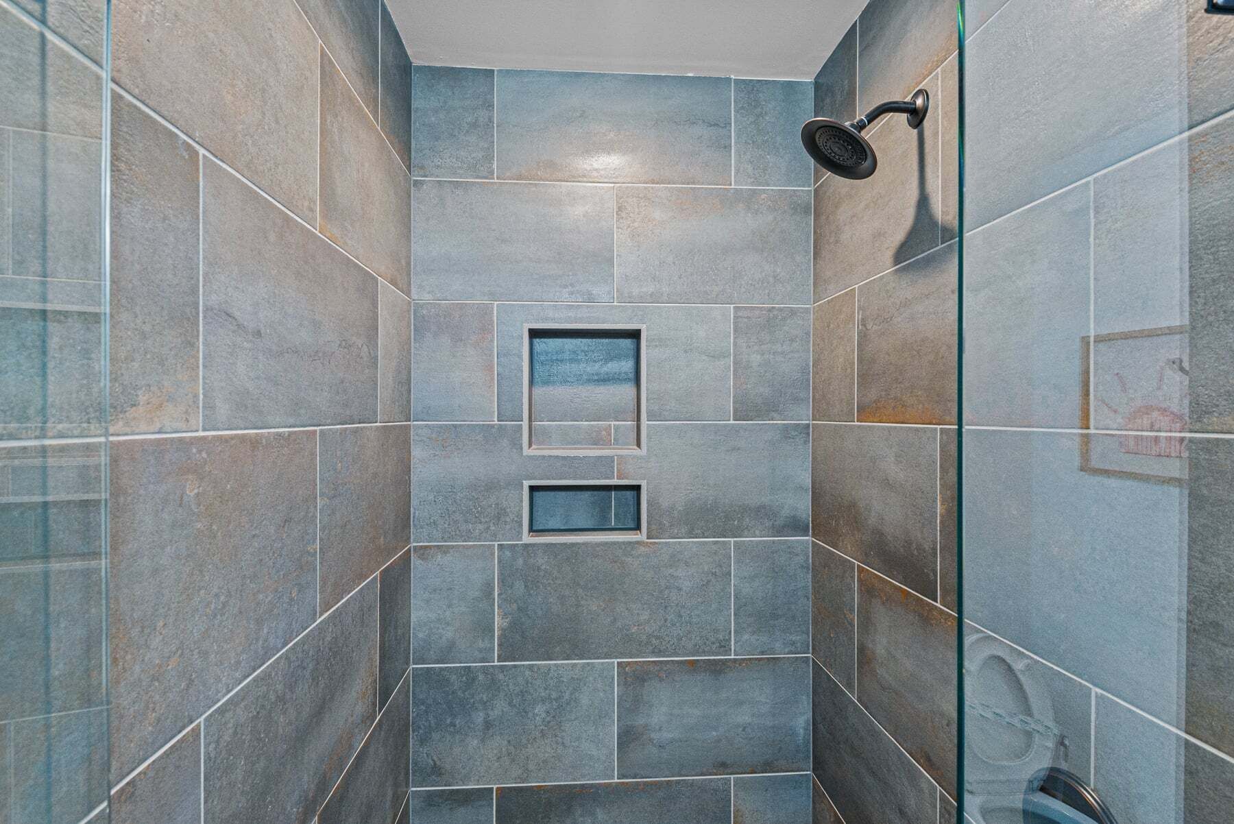 Una doccia con porta in vetro, soffione e parete rivestita di piastrelle con motivo geometrico.